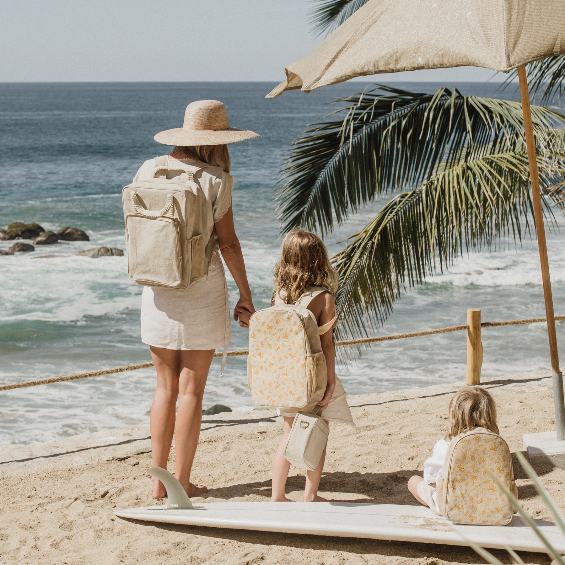 Woman wearing her backpack at the beach, holding ands with a young child