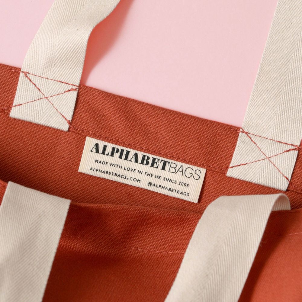 Close-up of a fabric bag with 'Alphabet Bags' label on a pink background