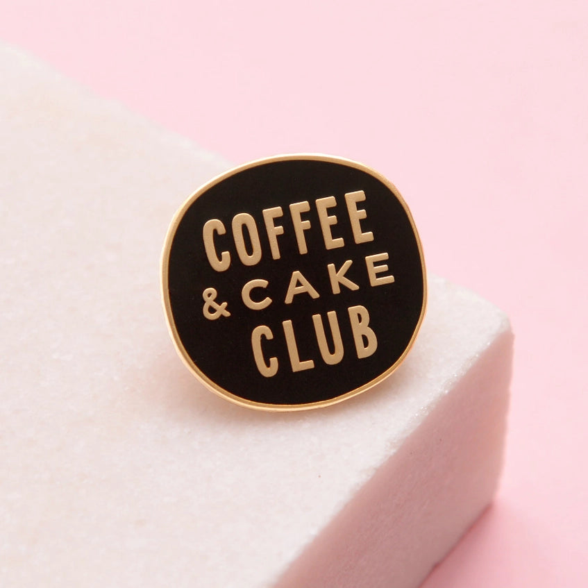 Black enamel pin badge with the words Coffee & Cake Club written in contrasting gold coloured metal.