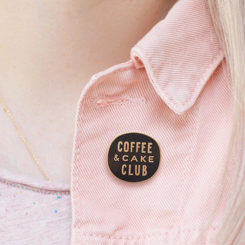 A close up of the pin badge on the lapel of a woman wearing a pale pink denim jacket.