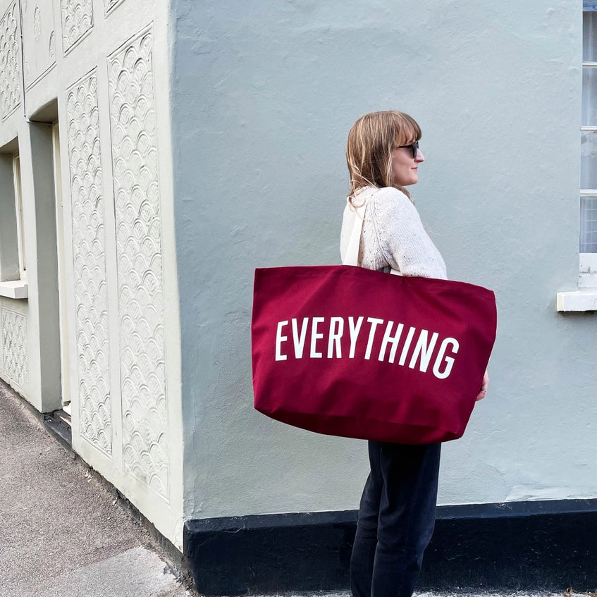 Woman standing on a street corner with the red canvas tote bag over her shoulder.