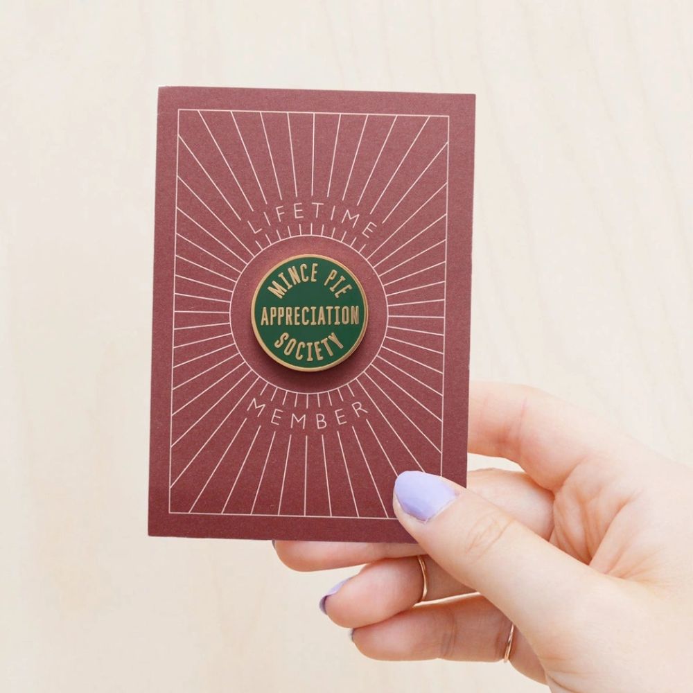 Green pin badge for the Mince Pie Appreciation society on a red cardboard backing with the words 'lifetime member'
