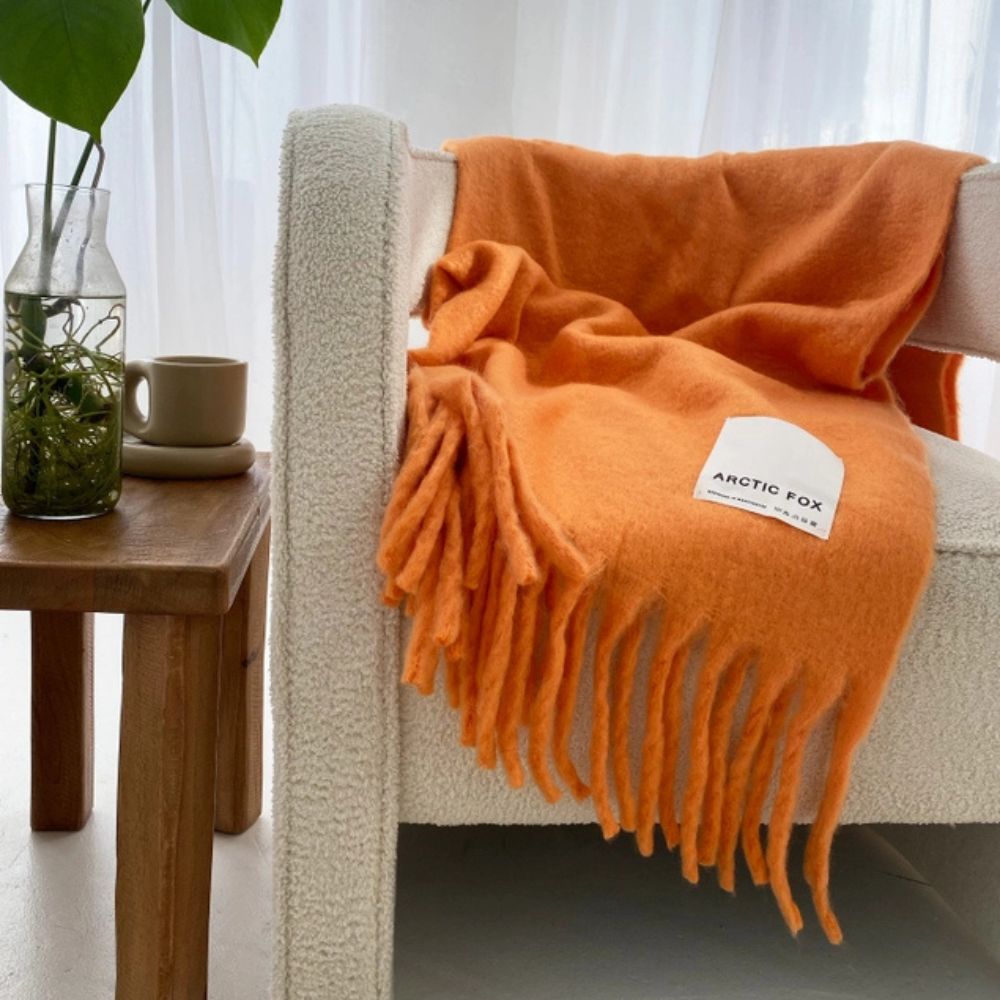 Orange throw with chunky tassels draped over a minimalist cream Scandi style chair