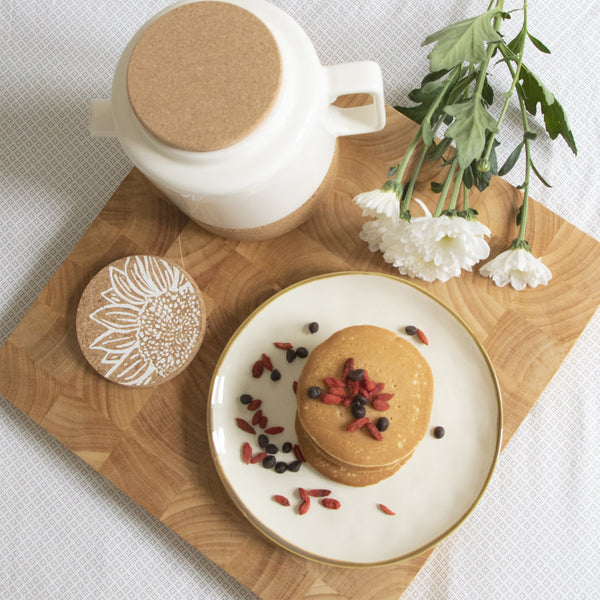 Large white teapot shown with plate of pancakes and sunflower coaster