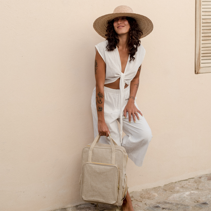Woman leaning against a wall holding her natural linen backpack by the top carry handle